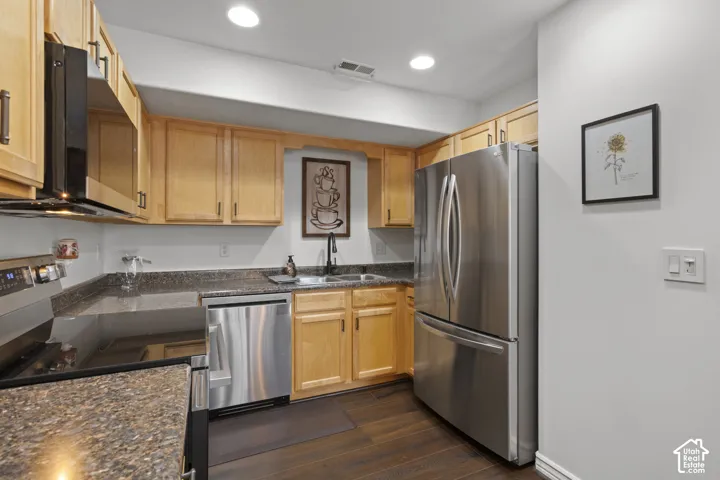 Kitchen featuring natural wood cabinetry, stone-finish countertops, stainless steel appliances, a dual-basin sink with a matte black faucet, and wood-finish flooring