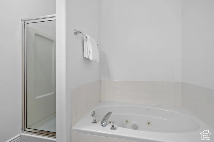 Jetted soaking tub with chrome-finish faucet hardware and surround tiling, accompanied by a stall shower featuring a glass door and metal frame