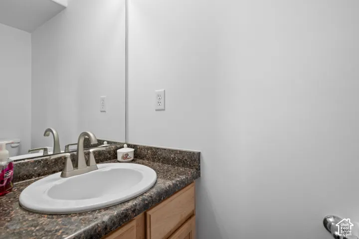 Bathroom vanity featuring a light wood-finish cabinet, stone-finish countertop, integrated oval sink, and a brushed nickel-finish faucet beneath a wall-to-wall mirror