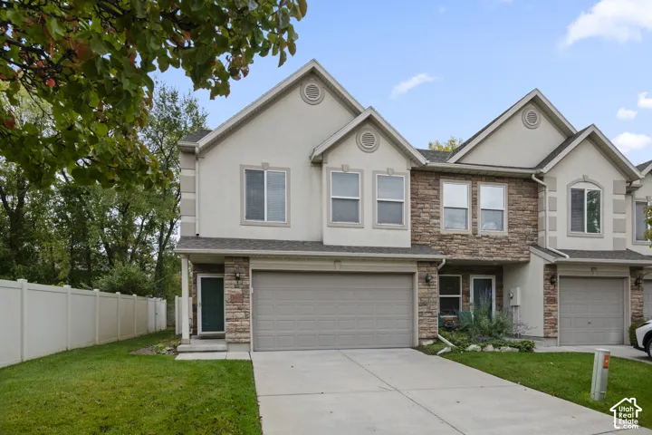 Multi-level exterior featuring stucco and stone veneer siding, an attached two-car garage, concrete driveway, and white vinyl perimeter fencing