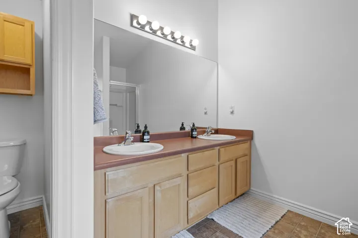 Double vanity with integrated sinks, neutral countertop, light-finish cabinetry, and full-width vanity mirror with integrated multi-bulb lighting