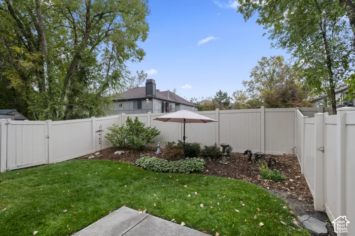 Fenced backyard featuring a concrete patio, mature trees, and a garden bed