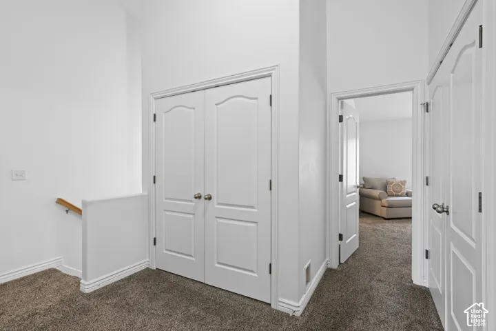 High-ceilinged corridor featuring double-panel interior doors, wall-to-wall carpeting, and wood-finish stair railing