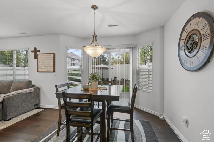 Dining area featuring dark wood-finish flooring, a pendant light fixture, three bay-style windows, and sliding glass patio doors with vertical blinds