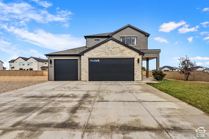 Two-story exterior featuring a stone facade, concrete driveway, and attached three-car garage with dark metal doors