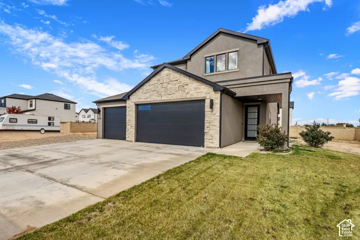 Two-story stucco exterior featuring stone veneer accents, multi-car garage with paneled doors, covered entryway, and concrete driveway