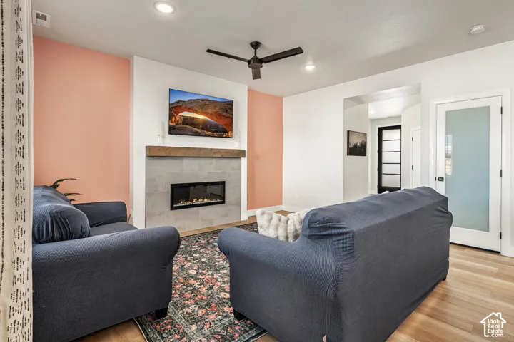 Linear fireplace with light-toned tile surround, wood-finish mantel, wood-finish flooring, recessed ceiling lighting, and frosted glass paneled door