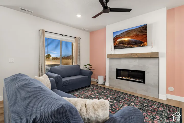 Living area featuring an electric fireplace with a floor-to-ceiling tile surround, natural wood mantel, recessed lighting, matte black ceiling fan, and wood-finish flooring
