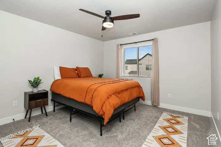 Neutral-toned bedroom featuring carpeting, a multi-blade ceiling fan with integrated lighting, and a single-pane sliding window