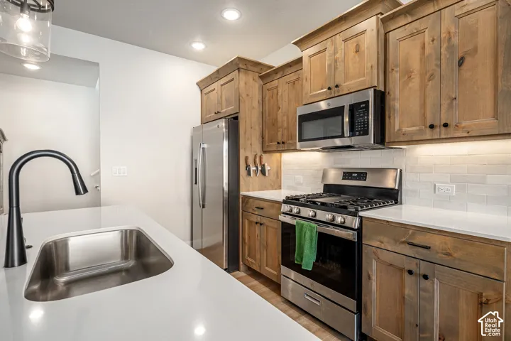 Kitchen featuring wood cabinetry, white countertops, a subway tile backsplash, stainless steel appliances, and a matte black gooseneck faucet