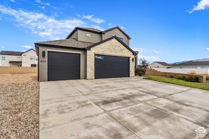Exterior featuring a neutral stucco finish, stacked stone accents, a three-car garage with dark metal doors, and a concrete driveway