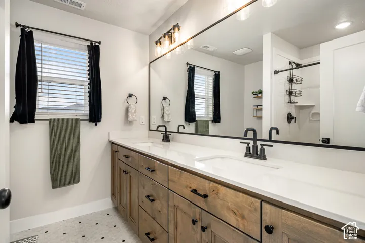 Bathroom vanity featuring wood-finish cabinetry, a white countertop with integrated dual basins, matte black hardware, and a large wall-mounted mirror