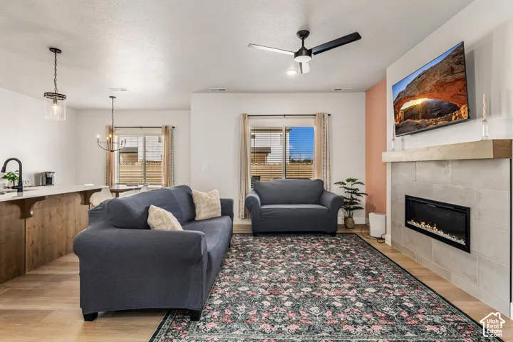 Living area featuring a floor-to-ceiling fireplace with tile surround, natural wood mantel, wood-finish flooring, and a contemporary ceiling fan