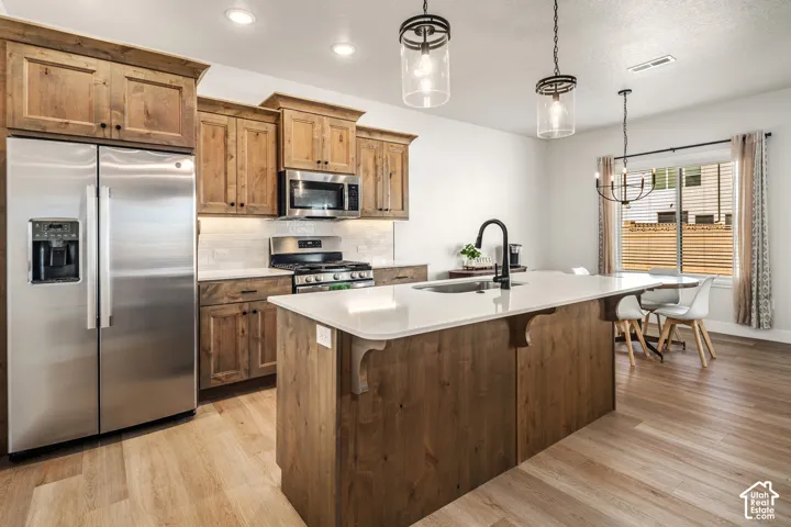 Kitchen featuring stained wood cabinetry, quartz-topped island with undermount sink, stainless steel appliances, and pendant lighting
