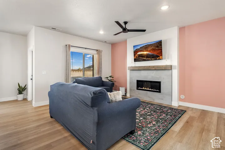 Living area featuring wood-finish flooring, a linear electric fireplace with stone-style surround, a wood-beam mantel, recessed lighting, and a ceiling fan