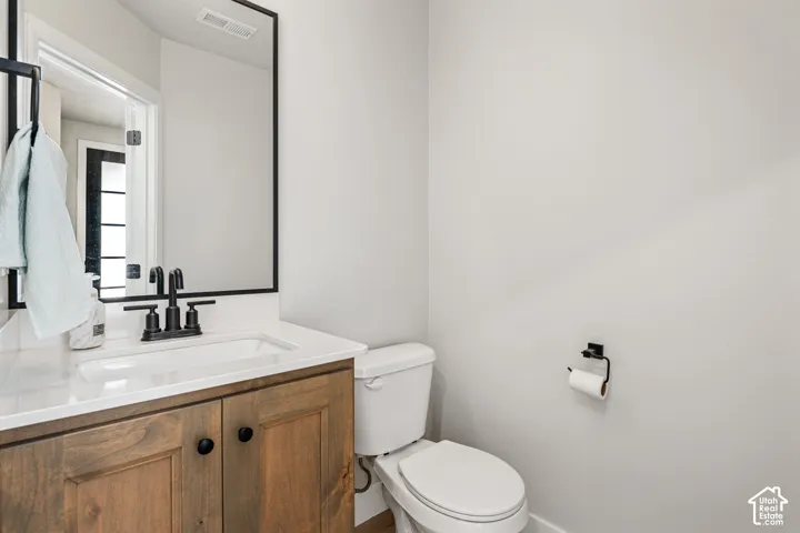 Wood-finish cabinetry featuring black hardware, white countertop with an integrated sink, matte black widespread faucet, and rectangular mirror with a matching black frame