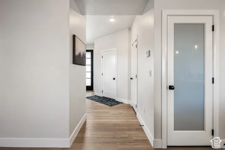 Interior hallway featuring wood-finish flooring, recessed lighting, and white interior doors with matte black hardware, including one door with a frosted glass pane