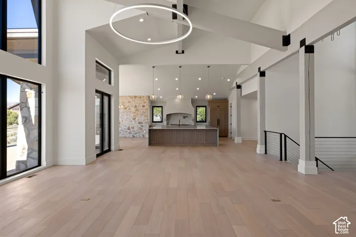 Open-concept interior featuring wood-finish flooring, vaulted ceilings with exposed structural beams, a stone-accent wall, a central kitchen island with cabinetry, and an oversized circular pendant light fixture