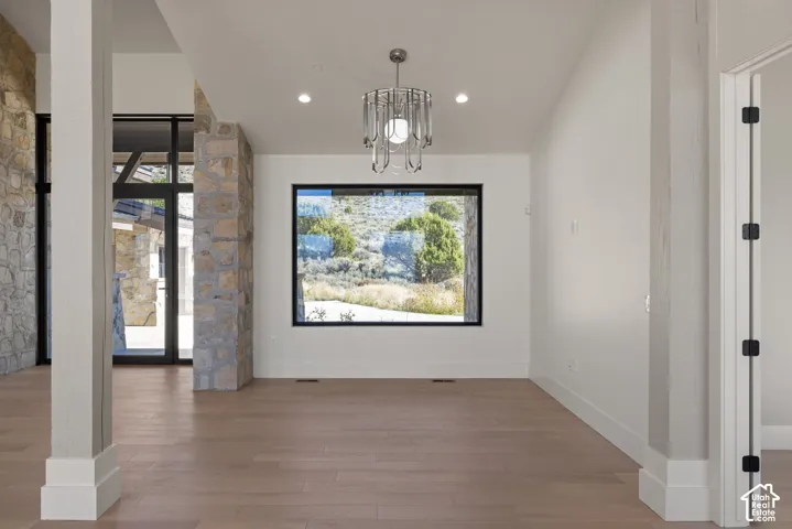 Interior space featuring wood-finish flooring, stone-clad structural columns, custom metal chandelier, large picture window, and recessed lighting