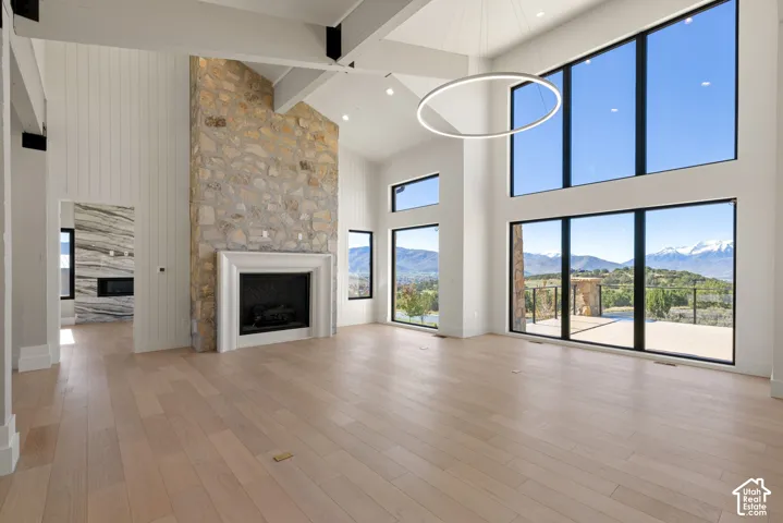 Vaulted ceilings with exposed beams, floor-to-ceiling stone fireplace, wood-finish flooring, oversized windows, and circular architectural lighting