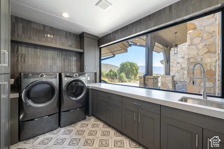 Utility room featuring custom dark cabinetry, quartz countertops, a stainless steel undermount sink with a gooseneck faucet, full-height tile backsplash, and patterned floor tile