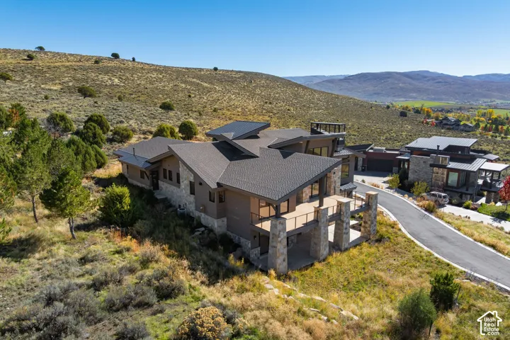 Modern custom residence featuring multi-level rooflines, stone and horizontal siding exterior, elevated deck with metal railing, and attached multi-car garage