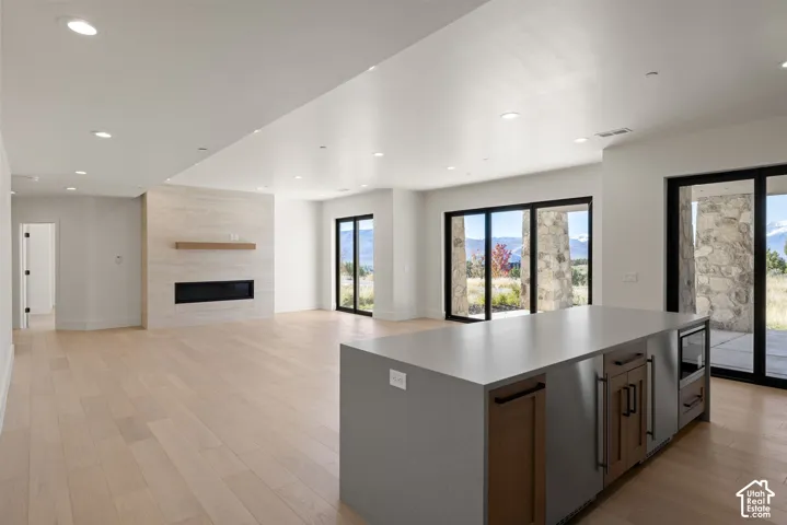 Open-concept floor plan featuring wood-finish flooring, recessed lighting, a stone-accented fireplace with a built-in mantel, and a kitchen island with stone surfacing
