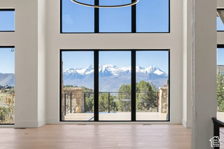 Double-height interior featuring floor-to-ceiling black-framed windows, wood-finish flooring, a modern circular pendant light, and mountain scenery