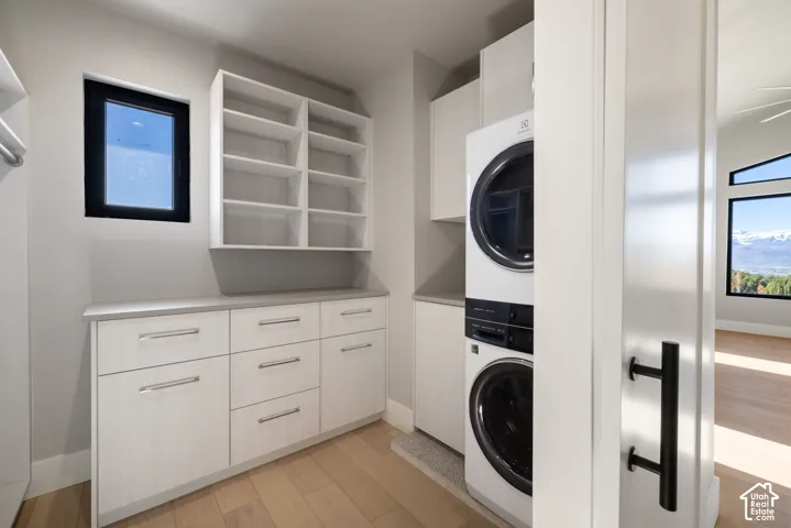 Laundry area featuring light-toned custom cabinetry, wood-finish flooring, open shelving, and a stacked washer and dryer unit
