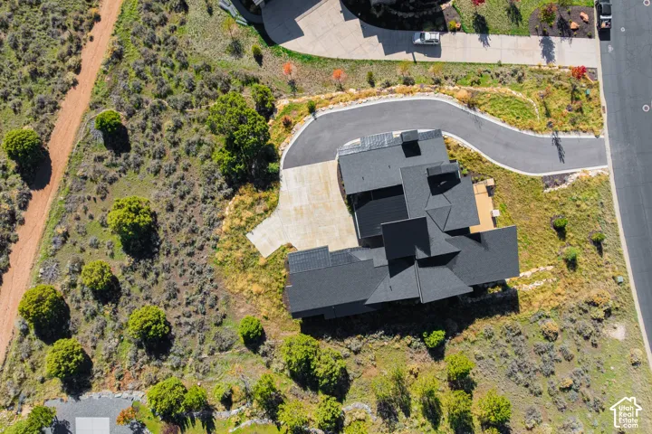 Aerial perspective of a multi-gabled architectural roofline, paved driveway, concrete parking apron, and expansive natural landscape