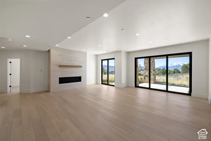 Open-concept interior featuring light wood-finish flooring, recessed lighting, a stone-surround fireplace with a wooden mantel, and floor-to-ceiling multi-panel sliding glass doors