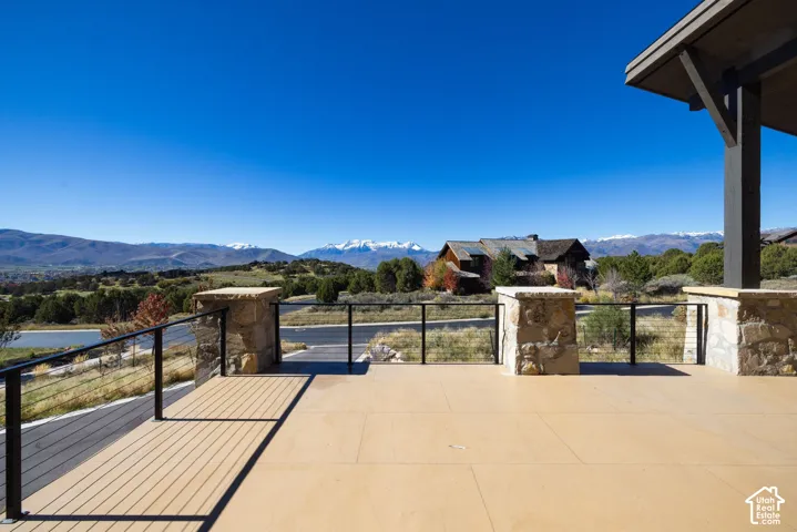 Covered exterior deck featuring smooth composite flooring, stone-clad pillars, and a metal cable railing system, overlooking a mountainous landscape