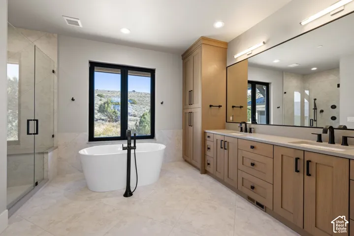 Freestanding soaking tub with matte black floor-mounted faucet, wood-finish cabinetry, quartz countertops, walk-in glass-enclosed shower, and large-format tile flooring