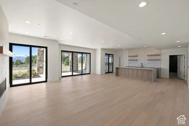 Open-concept interior featuring light wood-finish flooring, recessed lighting, expansive glass sliding doors, built-in cabinetry with stone-finish surfaces, and a stone-clad fireplace surround