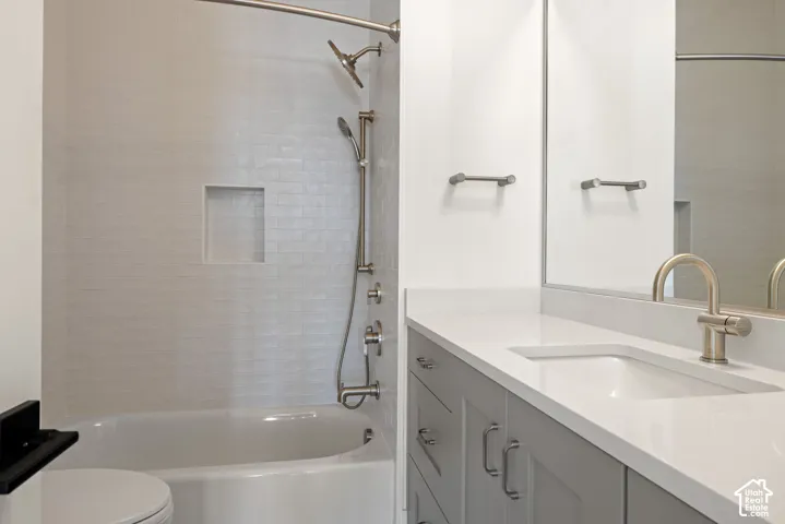 Bathroom featuring a tub-shower combination with white subway-tiled walls and a recessed niche, metallic handheld shower fixture, gray shaker-style vanity with solid-surface countertop, and a full-width wall mirror