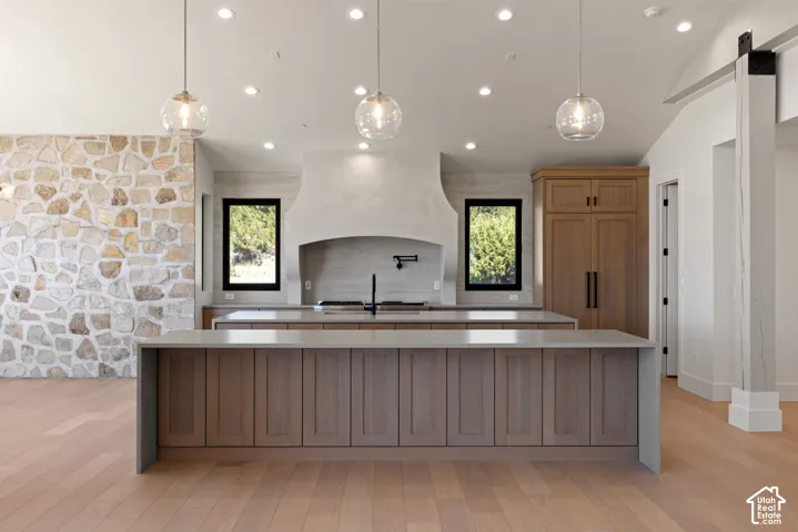 Kitchen featuring stone accent wall, dual islands with waterfall-edge countertops, custom cabinetry, recessed lighting, and glass pendant fixtures