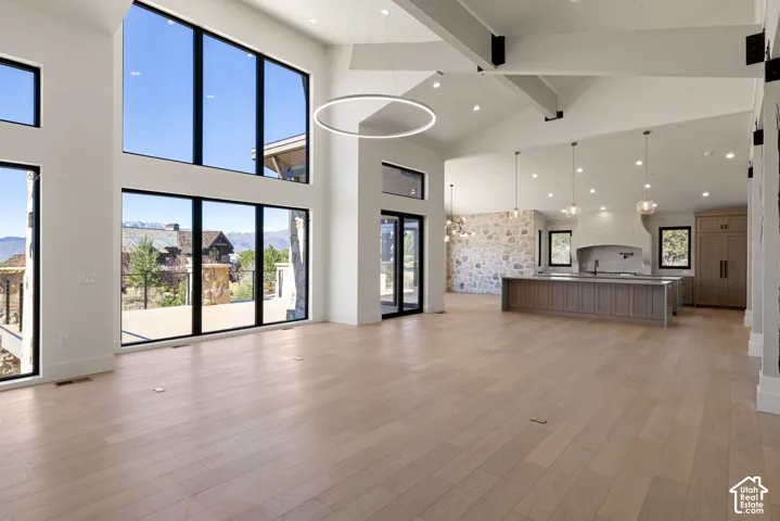 Vaulted ceilings with exposed beams, floor-to-ceiling windows, wide-plank wood-finish flooring, a kitchen featuring a stone accent wall, and a central island with integrated cabinetry