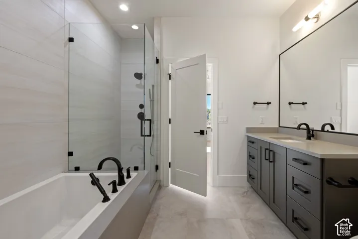 Bathroom featuring a dual-sink vanity with matte black hardware, stone-composite countertop, glass-enclosed shower, soaking tub, and large-format tile flooring