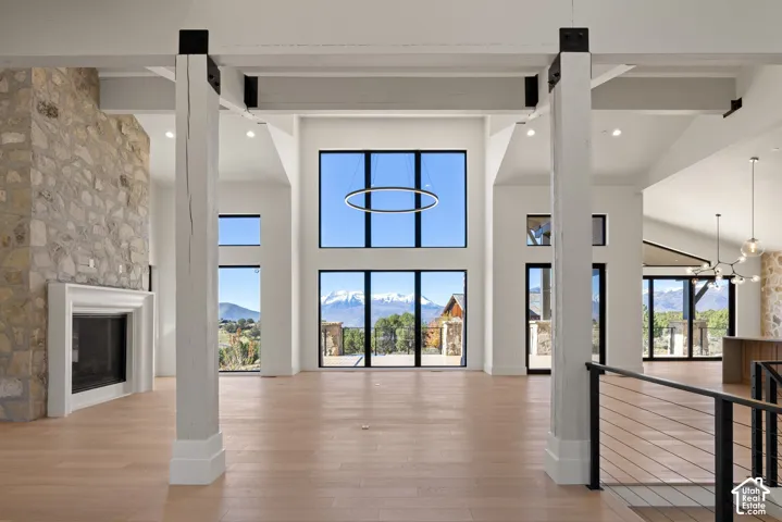 Vaulted ceilings featuring timber beams with metal hardware, floor-to-ceiling multi-pane windows, stone fireplace surround, and wood-finish flooring