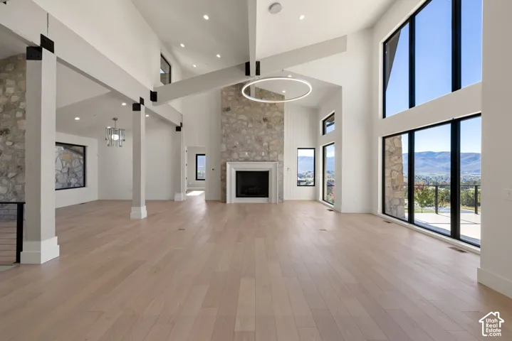 Open-concept interior featuring wood-finish flooring, vaulted ceilings with exposed beams, floor-to-ceiling stone fireplace, and expansive multi-story windows showcasing mountain scenery