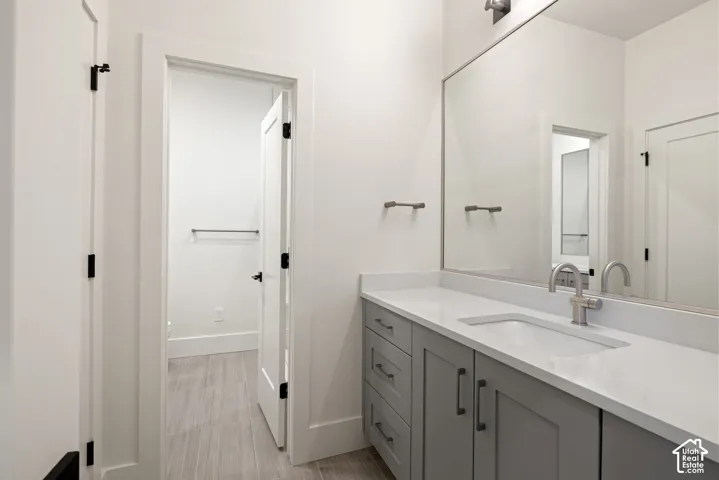 Bathroom vanity featuring gray shaker-style cabinetry, a white countertop with an integrated rectangular sink, a wall-to-wall mirror, and neutral tile flooring