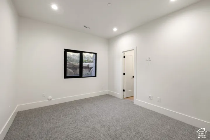 Neutral-toned carpeting, recessed ceiling lighting, a singular window with a black frame, and a solid-core interior door with black hardware