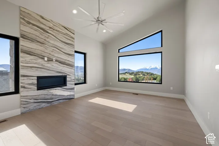 Vaulted ceiling featuring a linear fireplace with stone-finish surround, wood-finish flooring, multi-pane geometric windows, and a multi-blade ceiling fan