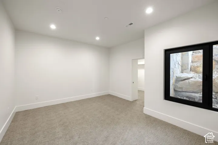Neutral interior space featuring carpeted flooring, recessed ceiling lighting, a walk-in closet, and a large window with a black frame looking onto a natural stone retaining wall
