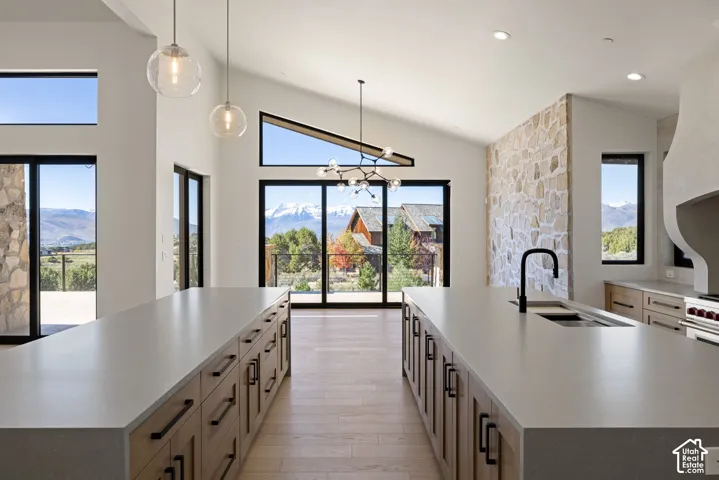 Dual islands with solid-surface countertops, vaulted ceilings, floor-to-ceiling stone accent wall, multi-pane floor-to-ceiling windows, and wood-finish flooring