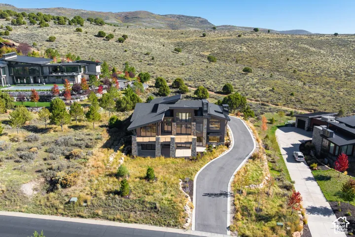 Contemporary residence featuring a multi-gabled roofline, stone veneer siding, expansive glass windows, an elevated deck, and a private asphalt driveway