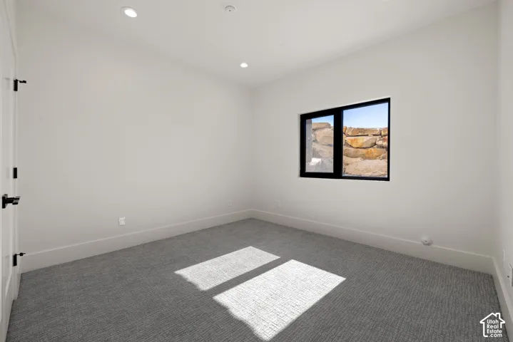 Room featuring neutral carpeting, recessed lighting, and a window with black trim highlighting a natural rock retaining wall