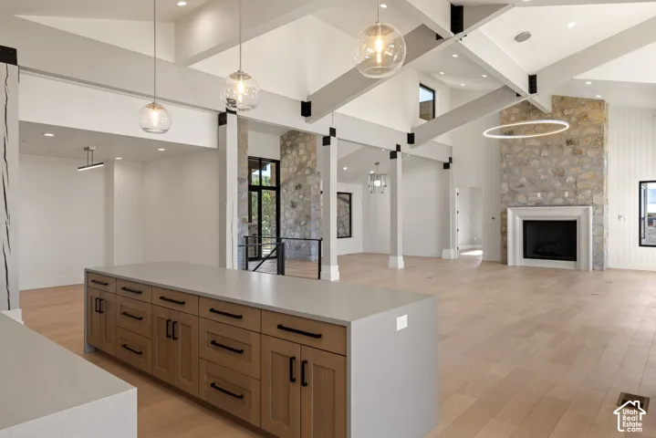 Open-concept living space featuring vaulted ceilings with exposed beams, stone-clad fireplace, wood-finish flooring, and a kitchen island with quartz countertops and custom cabinetry