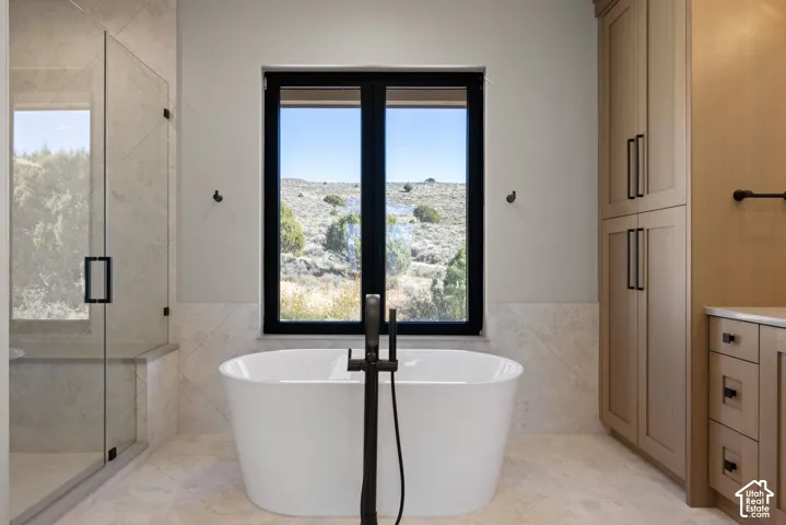 Freestanding white soaking tub with matte black floor-mounted faucet, glass-enclosed shower with tiled surround, and floor-to-ceiling wooden cabinetry with matte black hardware