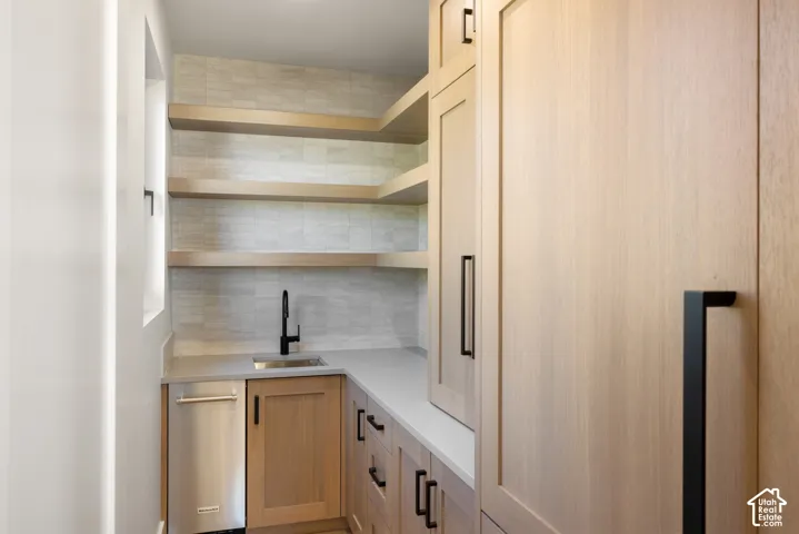 Custom cabinetry featuring wood-finish cabinetry, matte black hardware, stone-finish countertops, floating wood shelves, and a stainless steel sink with a matte black faucet